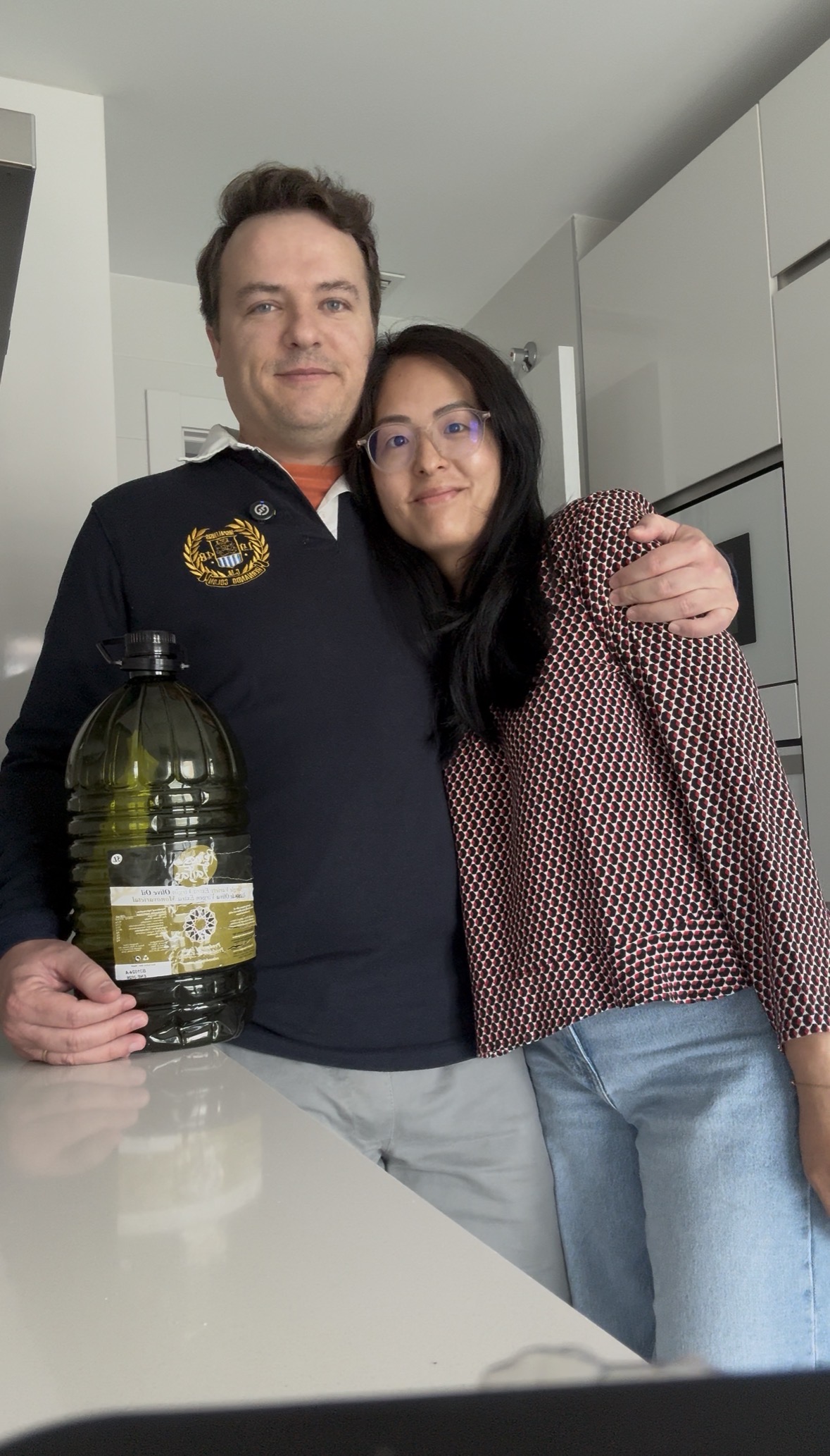 Arbequina 15L (3×5L) · Alfanje 6 una pareja posando con una botella de aceite de oliva de 5 litros